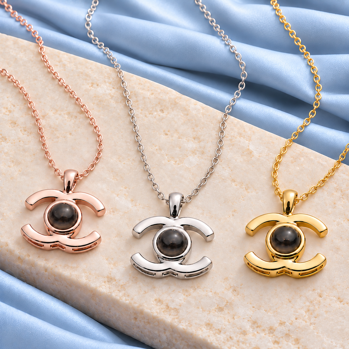 Drei 4MyLove Fotoketten Augenblick in Roségold, Silber und Gold mit dunkler Projektionslinse auf hellem Stein und blauem Stoff
