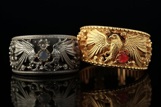Zwei kunstvoll gearbeitete Armreifen mit filigranem Vogel-Motiv in Silber und Gold vor spiegelndem Untergrund