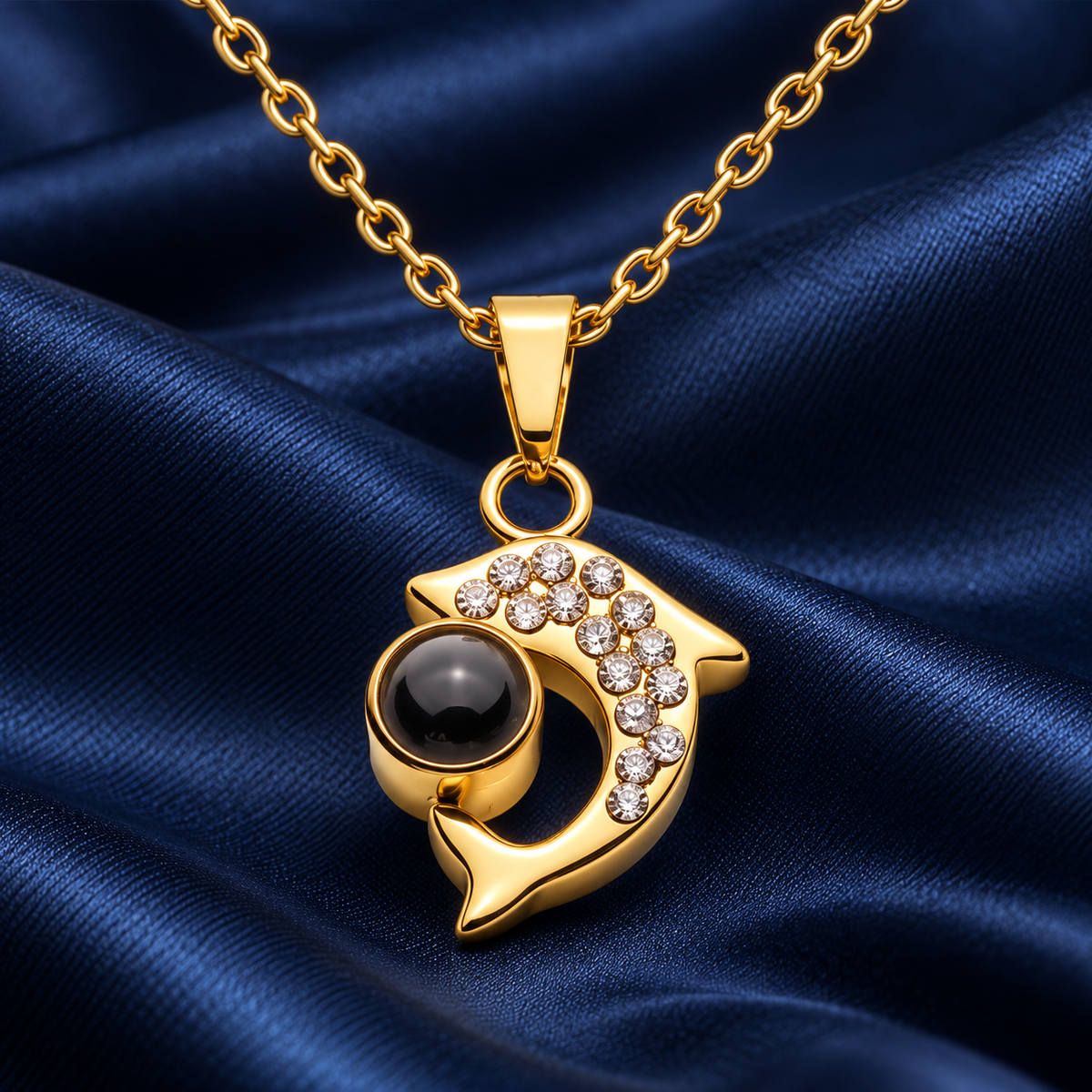Goldfarbene Delfin-Fotokette von 4MyLove mit Kristallen und dunkler Fotolinse auf blauem Satin.