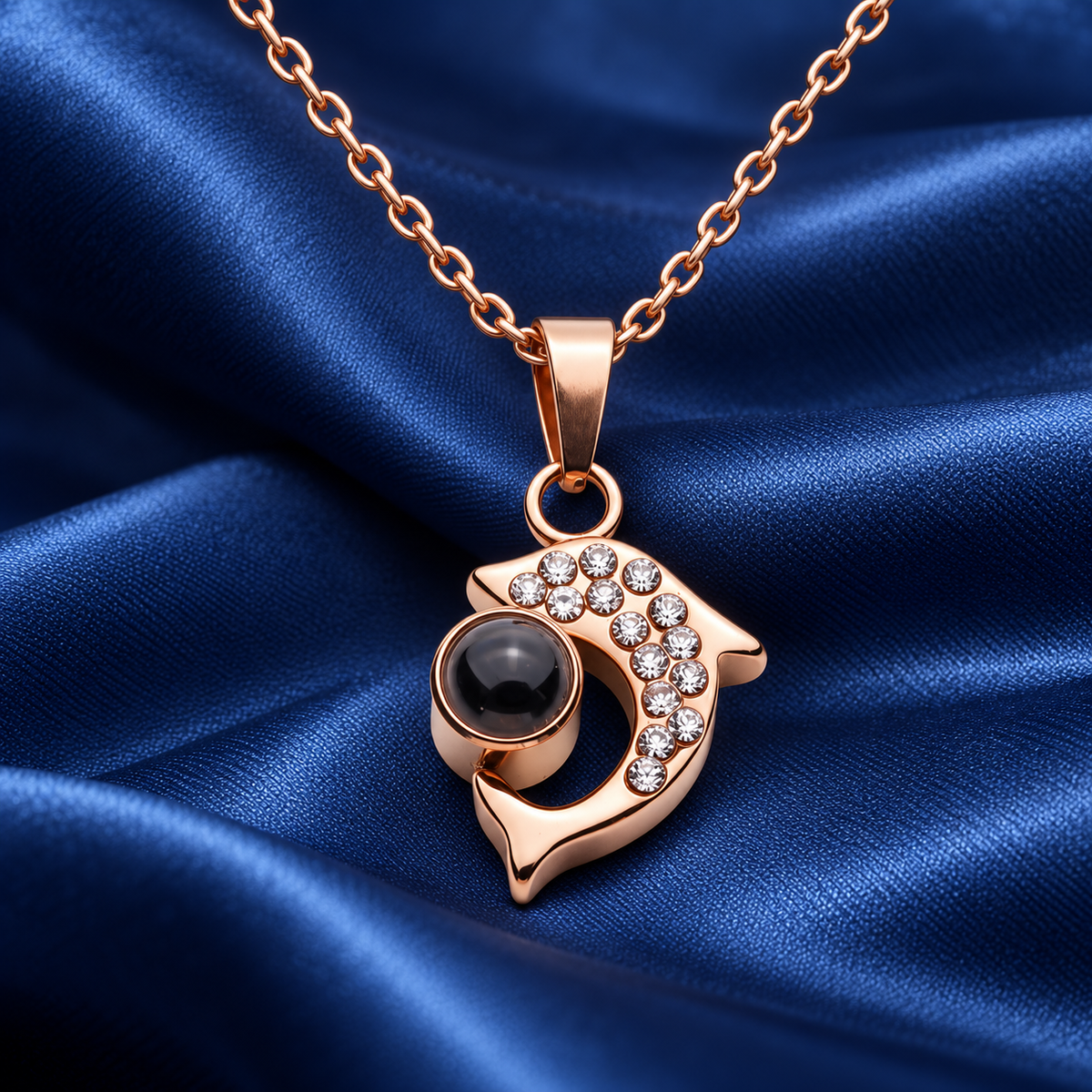 Roségoldfarbene Delfin-Fotokette von 4MyLove mit Kristallen und dunkler Fotolinse auf blauem Satin.
