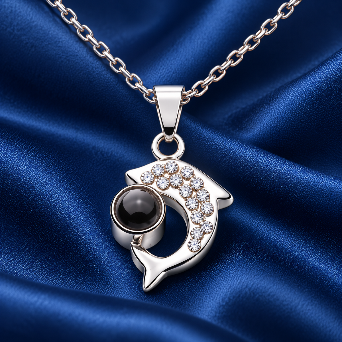 Silberfarbene Delfin-Fotokette von 4MyLove mit Kristallen und dunkler Fotolinse auf blauem Satin.