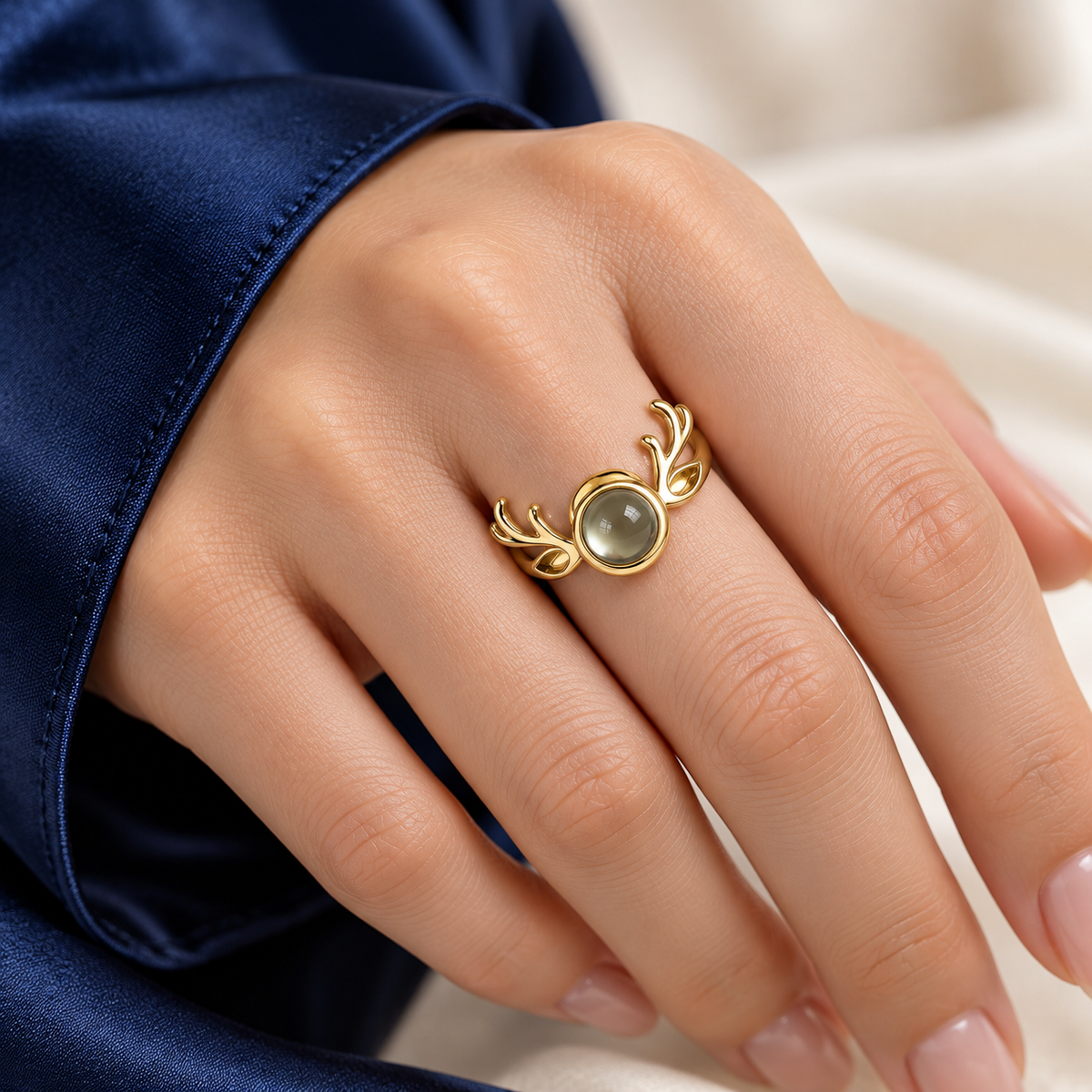 Hand mit goldenem Geweihring und Fotolinse vor dunkelblauem Ärmel