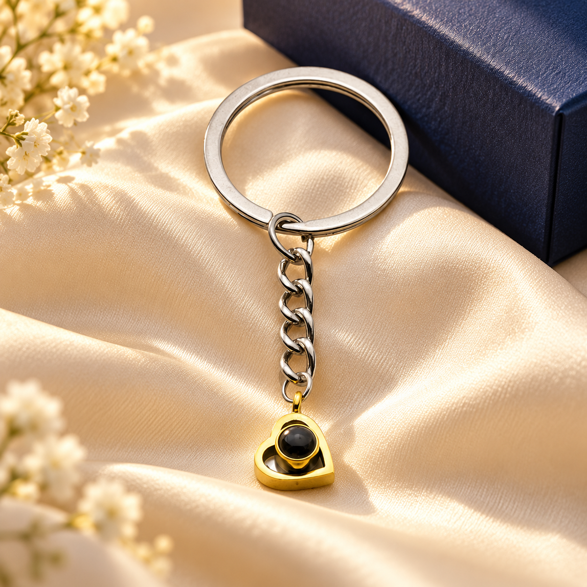 Schlüsselanhänger mit Foto: goldenes Herz mit Linse an Gliederkette vor einer Geschenkbox