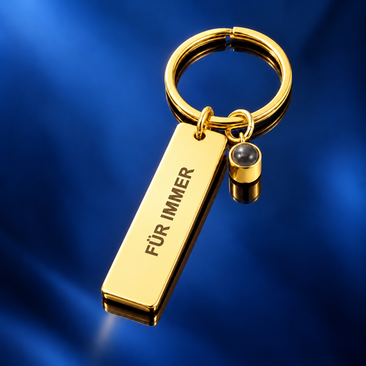 Goldener rechteckiger Schlüsselanhänger mit Gravur „Für immer“ und Fotolinse auf dunkelblauem Satin