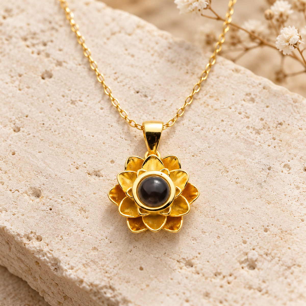 Goldfarbene Blumenkette von 4MyLove mit mehrlagigem Blütenanhänger und dunkler Fotolinse auf hellem Naturstein.